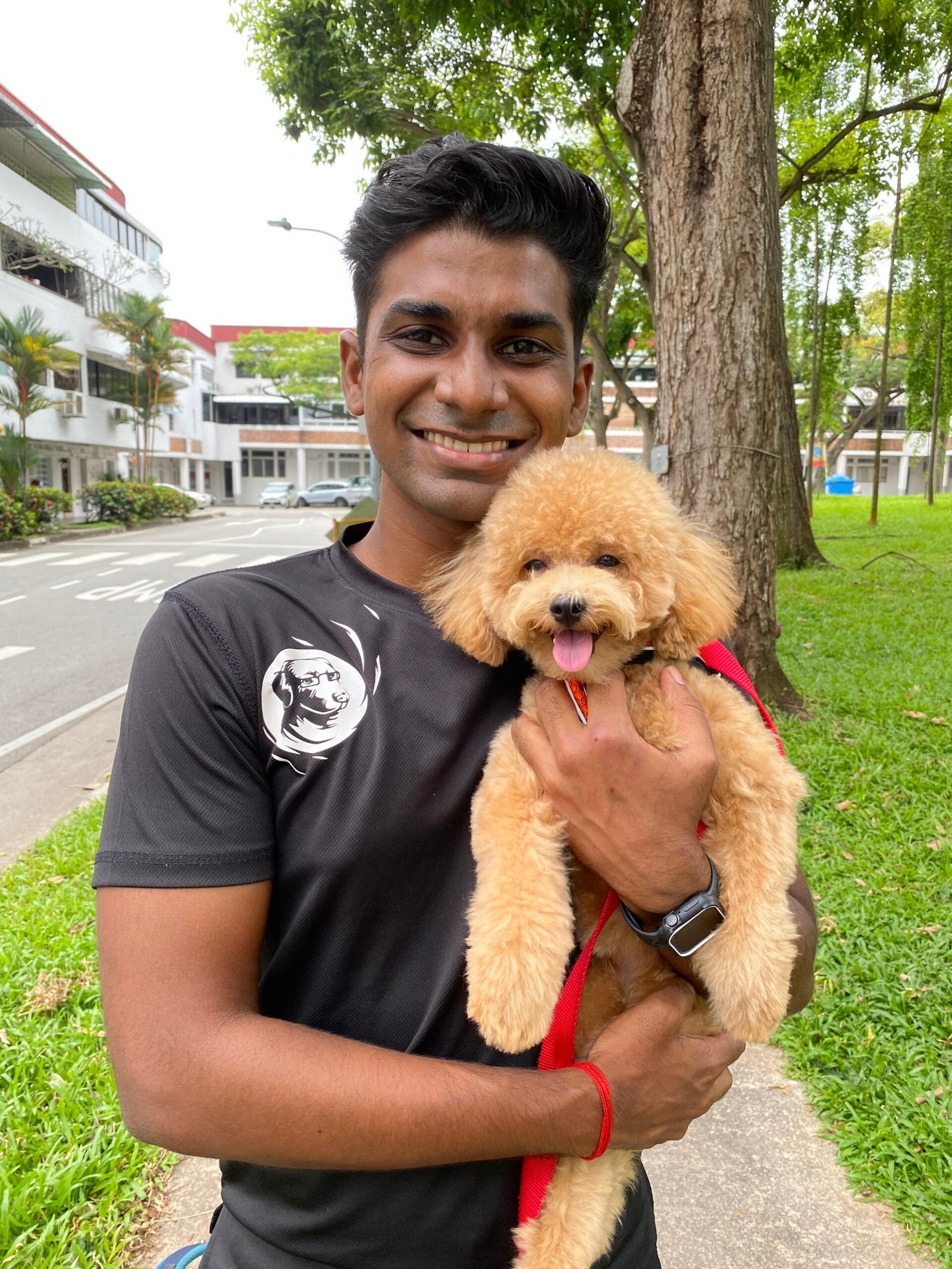 A smiling dog trainer holding Charlie, a happy apricot poodle, during an outdoor walk in Singapore.